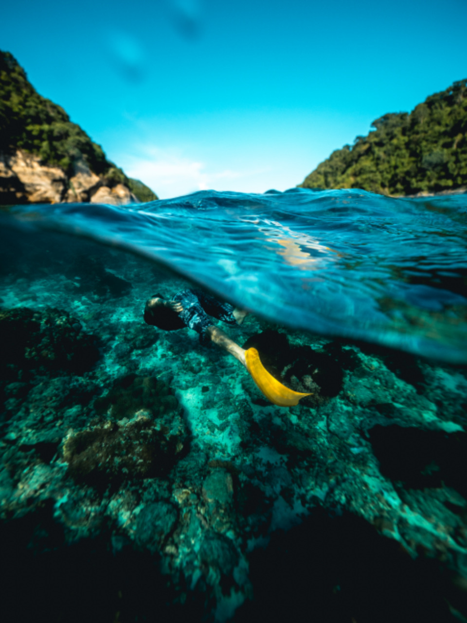 A split above/below-water view of a snorkeller near an island