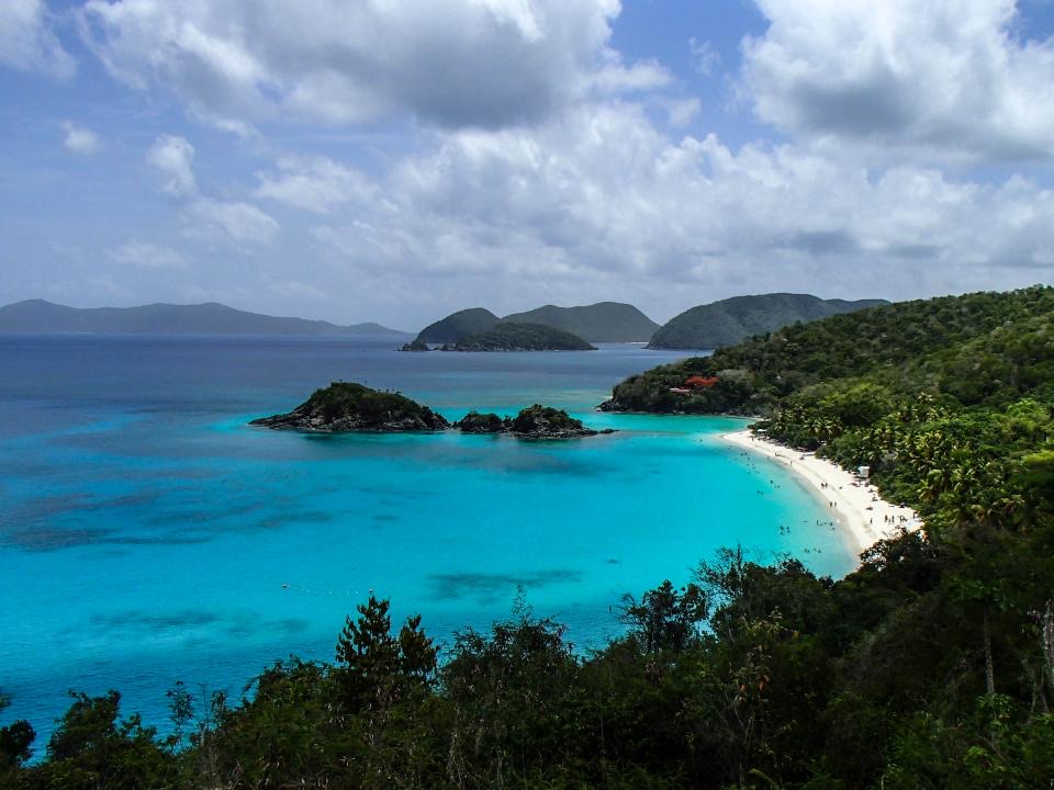A turquoise bay with small islands and a curved beach, seen from a hill