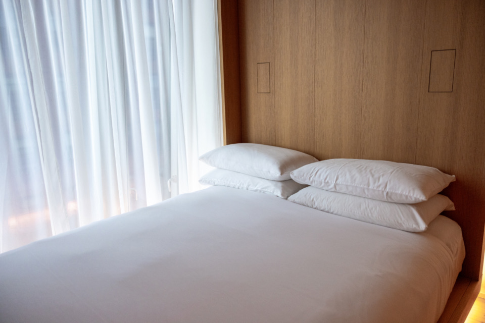 A white bed in front of sheer curtains in soft daylight