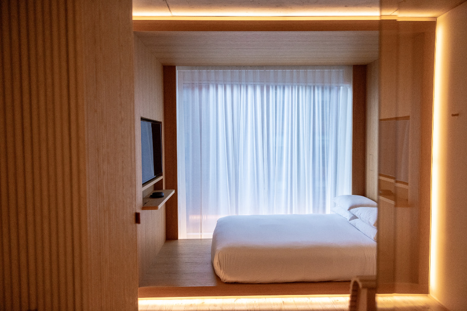 A timber-lined bedroom with white curtains and warm lighting